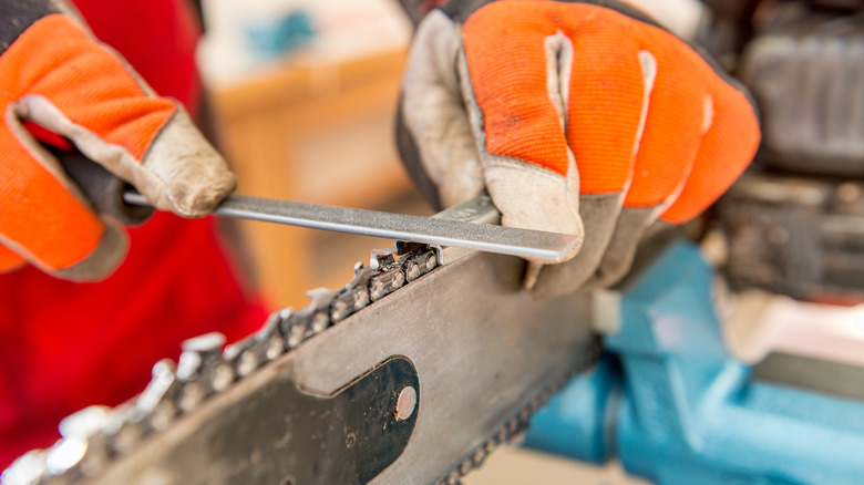 Gloved hands sharpening chainsaw blade with metal file