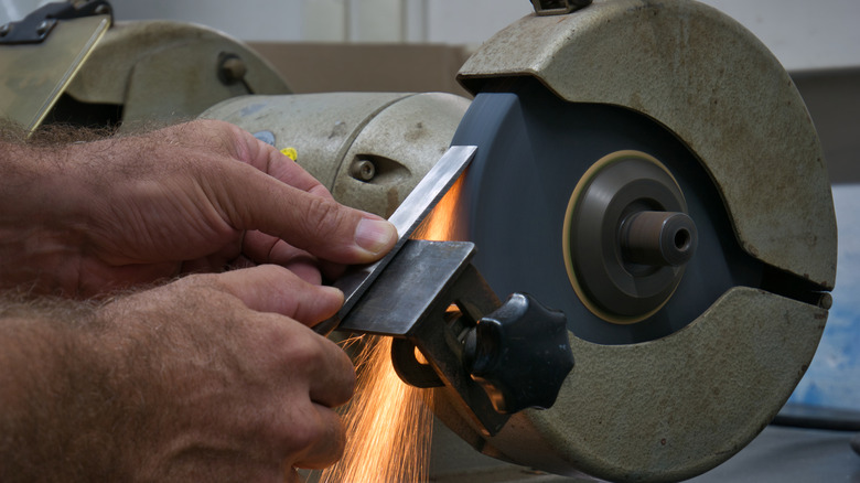 Hands sharpening a chisel using a bench grinder