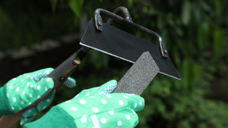 Gloved hands sharpening a garden hoe blade with a metal file
