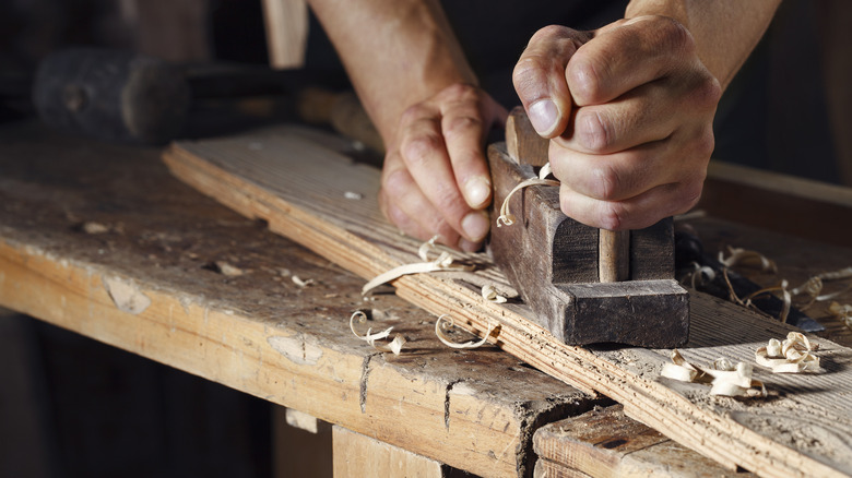 Carpenter using a hand plane on a piece of word, with shavings scattered around it