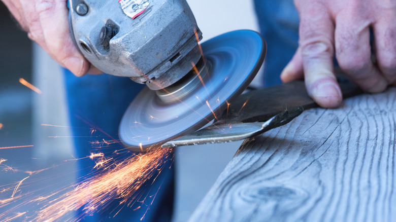 Angle grinder sharpening a lawn mower blade propped on a wood railing