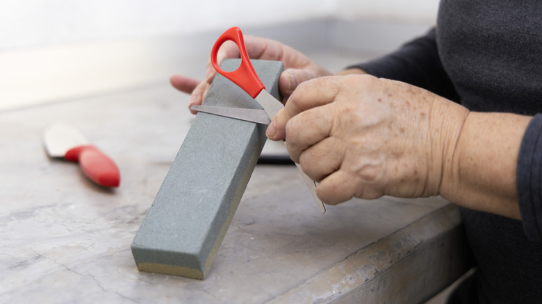 Hands sharpening a pair of red scissors on a whetstone