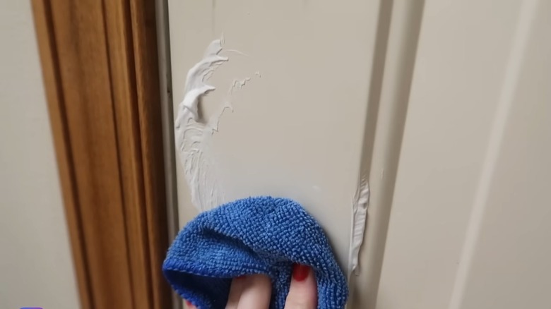 A person rubbing shaving cream onto a painted cabinet