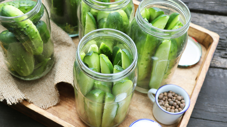 Pickles sitting inside clear jars on a wooden tray