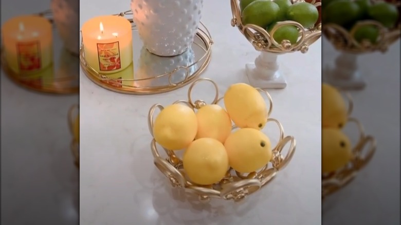 Fruits in golden decorative bowls beside a golden tray with a lit candle and white planter