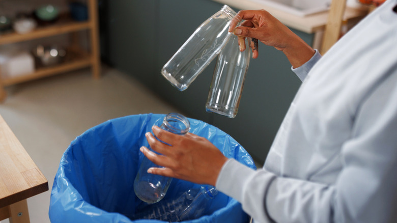 a woman is taking empty glass bottles out of the recycling bin