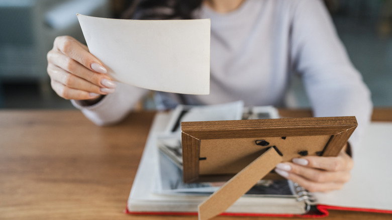 A woman holding a photo and picture frame while sitting at a desk. You cannot see her face