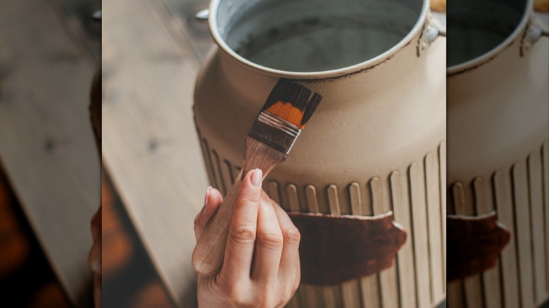 A person with a paint brush painting a metal milk jug