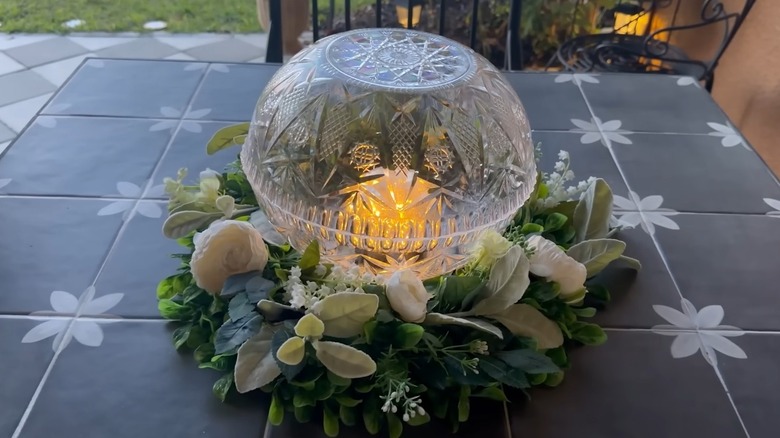 A light globe placed in the middle of a flower wreath on a patio table