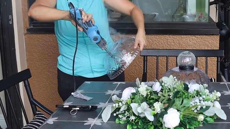 Woman cutting a hole in the bottom of a punch bowl with other craft supplies placed on her patio table