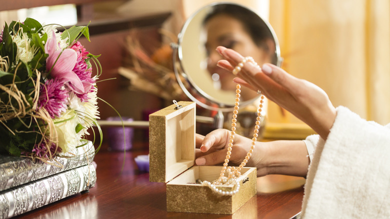 A woman takes out long necklaces from a jewelry box