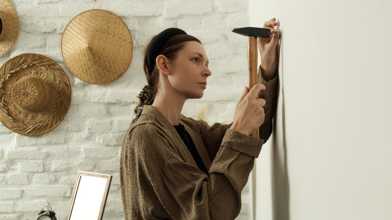 Woman hammering small nail into white wall for hanging wall decor