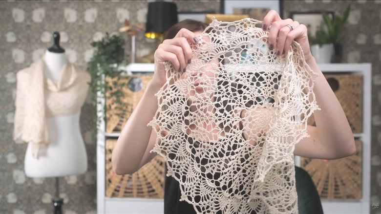 A young woman holding up large lacey doily in stylish crafting room