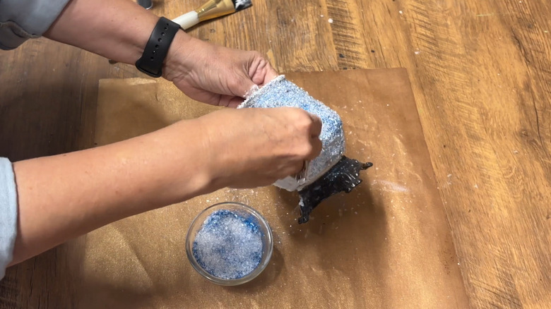 A hand sprinkling Epsom salt and glitter onto a vase