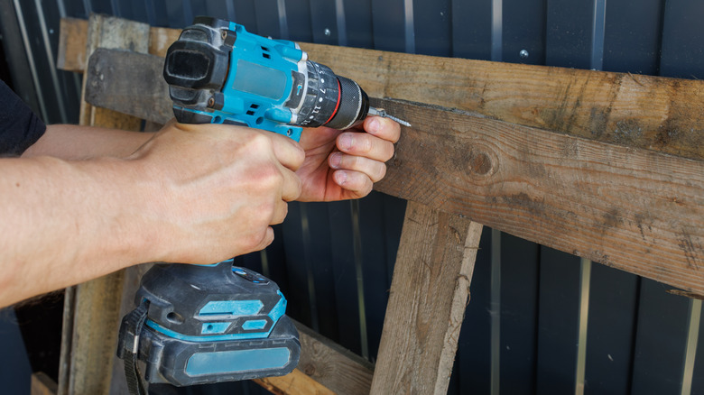Person using cordless screwdriver on wooden pallet