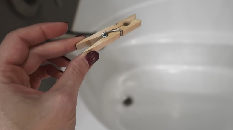 Hand holding clothespin over bathtub