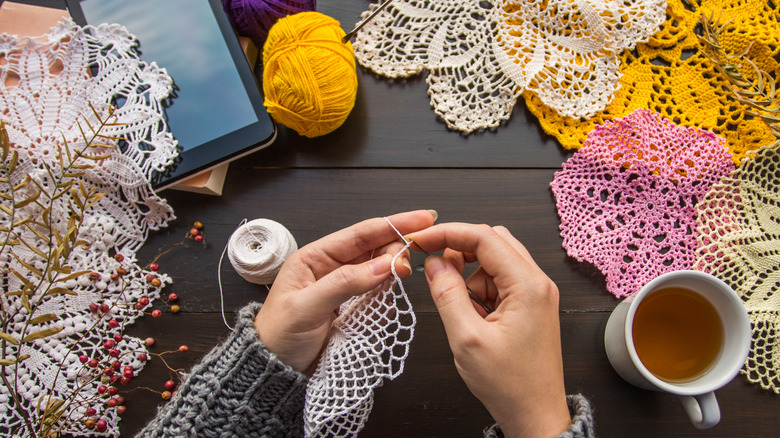 A person knitting a doily with other doilies around