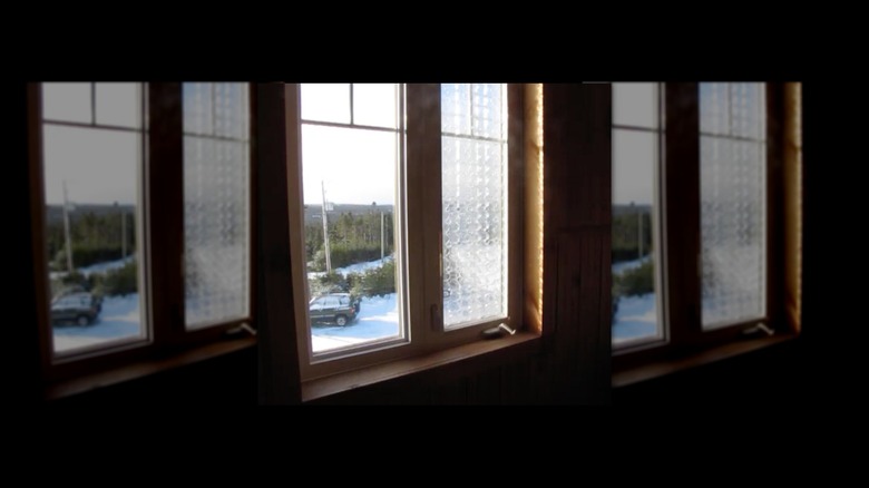 Two window panes, one clear and one covered with plastic egg cartons. Winter snow seen outside window, sunlight streaming in.