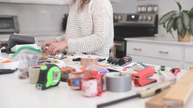 person sorting through random junk drawer items on kitchen countertop