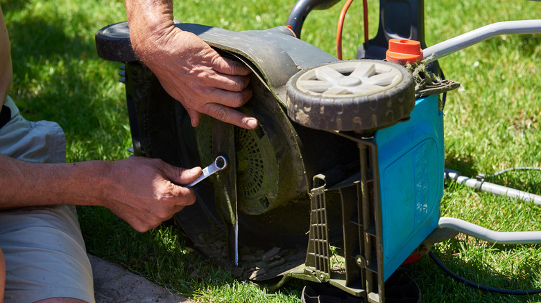 Person removing lawnmower blade out in a grassy yard