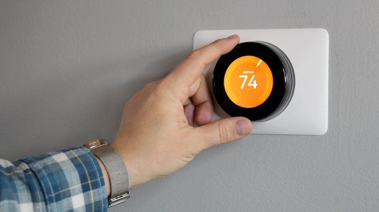 Someone's hand adjusting a smart thermostat on a gray wall