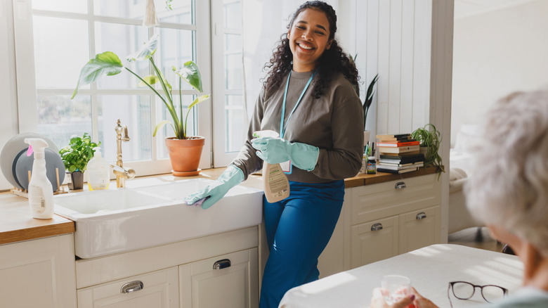 A young woman smiles at an older person while cleaning the kitchen sink.