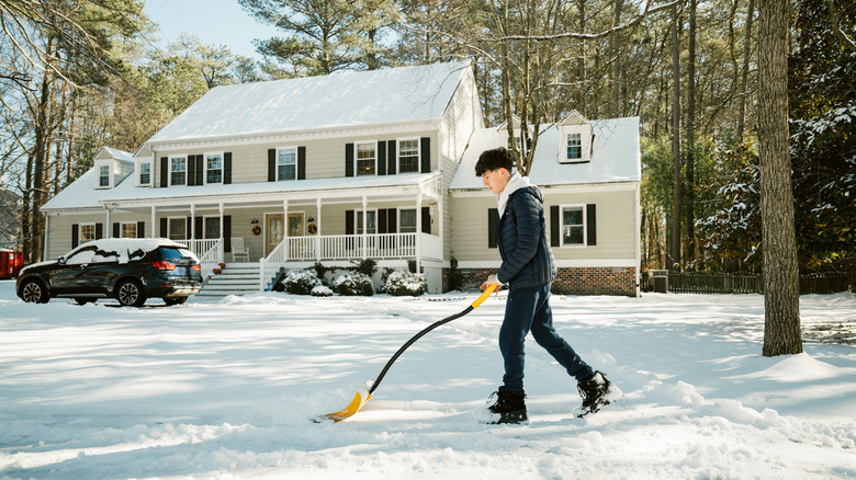 Young man moving snow off of a driveway with a yellow shovel