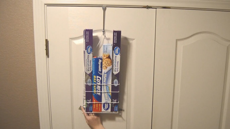 Organized kitchen aluminum foil, plastic wrap, and parchment paper organized on hanging shower caddy over pantry door in ktichen