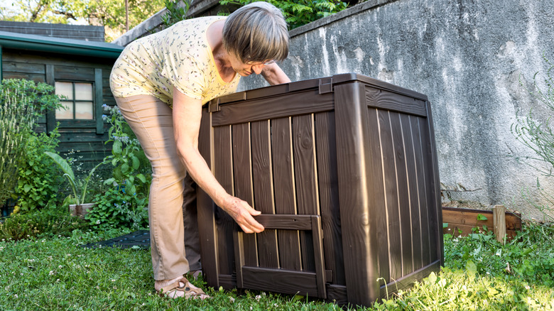 A woman in the backyard trying to move a deck box