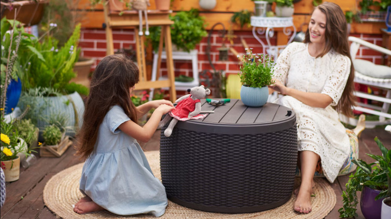 A grey outdoor storage ottoman doubling as a table with with a woman and child sitting at it