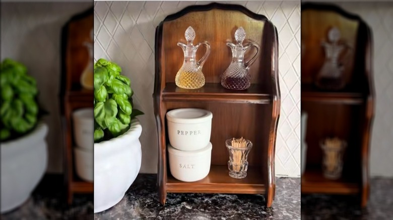 A small shelf sitting on a kitchen countertop with bottles of oils, jars of seasonings, and toothpicks