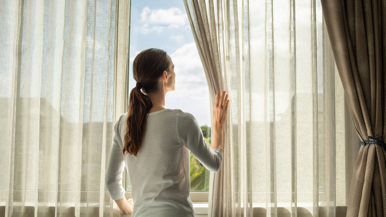 Woman sliding curtains and drapery to the side