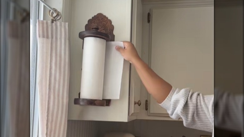 Person grabbing a paper towel from a vintage wooden paper towel rack mounted on the side of a cabinet
