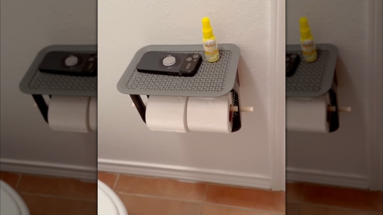 A smartphone and potpourri spray bottle sit on the shelf of a Dollar Tree DIY toilet paper holder