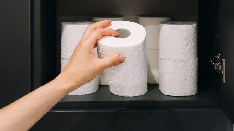 A hand puts toilet paper rolls in a black cabinet