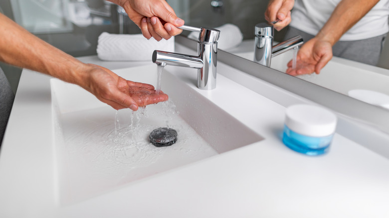 Person washing hands over a white solid surface sink