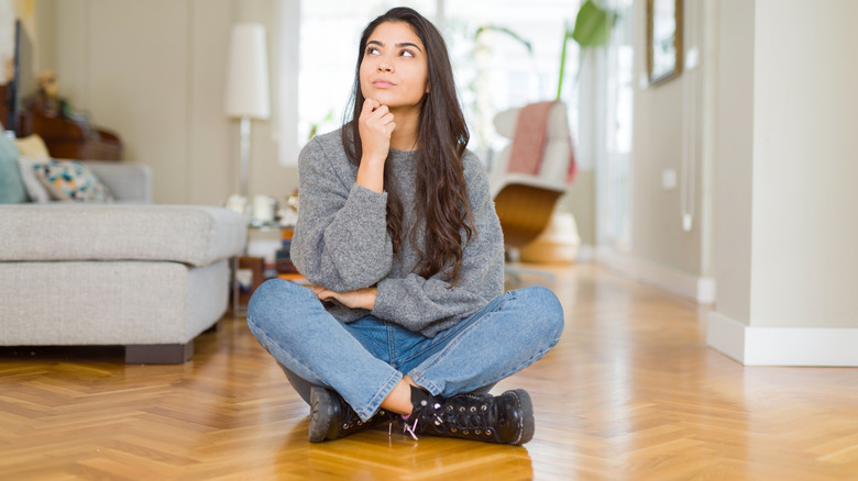 A woman sits on hardwood flooring, thinking