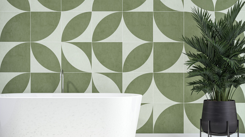 Green geometric wallpaper with white bathtub and potted plant.
