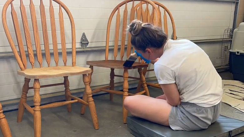 Young woman in casual clothes adding finish to gel-stripped honey oak wood chairs