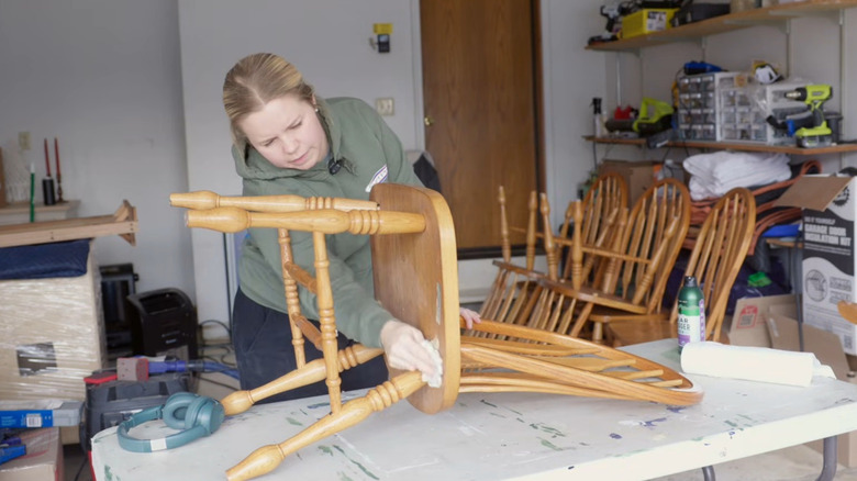 Blonde woman preparing vintage honey oak chairs for DIY update project in home garage