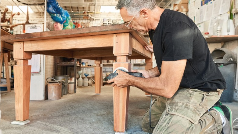 Man sanding dated wood coffee table in workshop