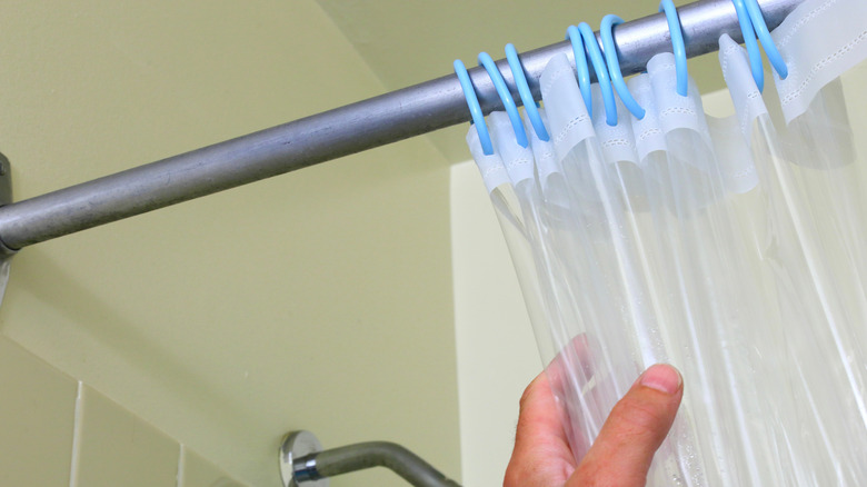 Person reaching up and grabbing a clear plastic shower curtain