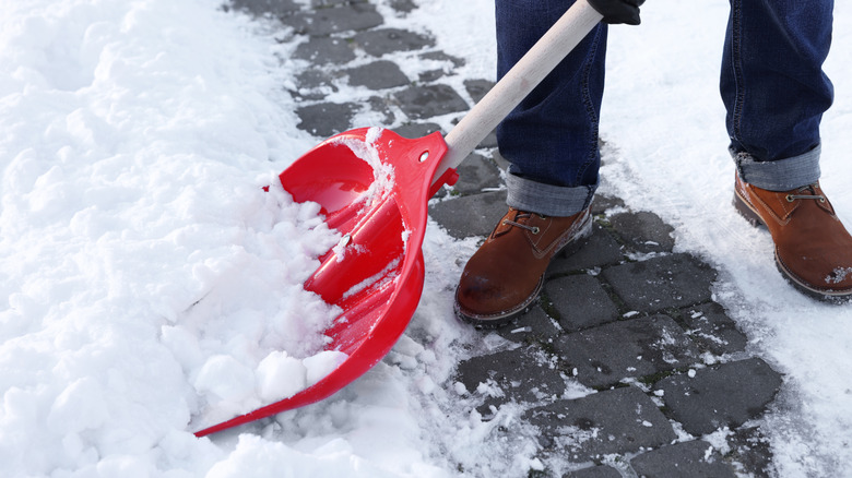 A person shoveling snow from a brick path with a red shovel