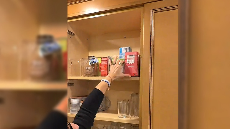 Person reaching to grab a clear bin off of an upper shelf in a tall cabinet