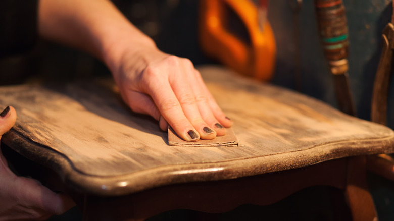 A hand with painted nails sanding an old wood table