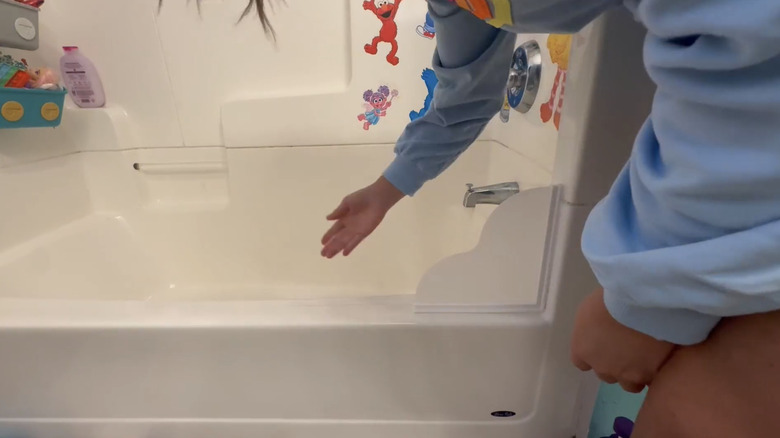 A person running a bath with a guard on the corner of the tub