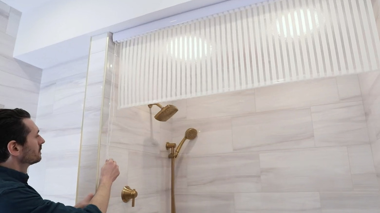 A person rolling up a roller-blind style shower curtain over a bath