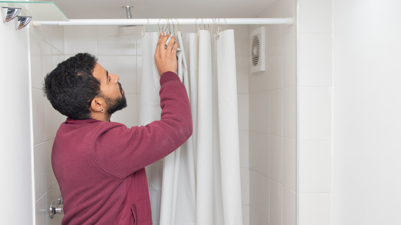A person adjusting a white shower curtain on a suspension pole