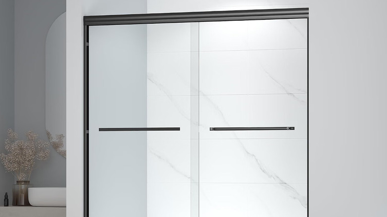 A bathroom with marble tiling and a sliding door across the bathtub with black rims