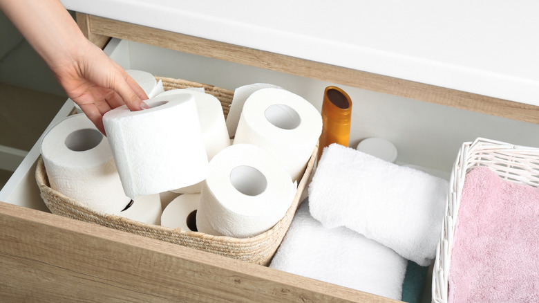 person taking toilet roll from drawer in bathroom